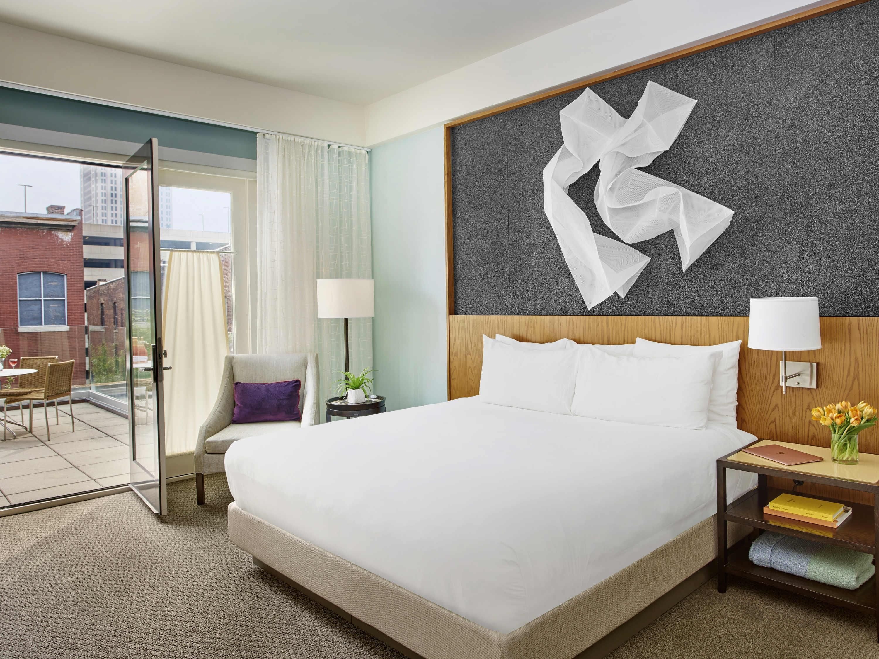 Habitaci ón de hotel con una cama grande, una mesita de noche con lámpara, una silla y vistas al exterior.