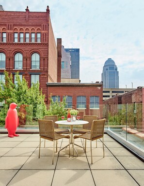 A rooftop terrace with a round table, wicker chairs, a red sculpture, and a view of city buildings. - 21c Museum Hotel Louisville (Louisville)