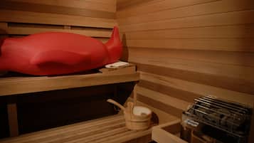 A sauna with wooden benches, a red massage chair, a wooden bucket, and a metal rack with towels.
