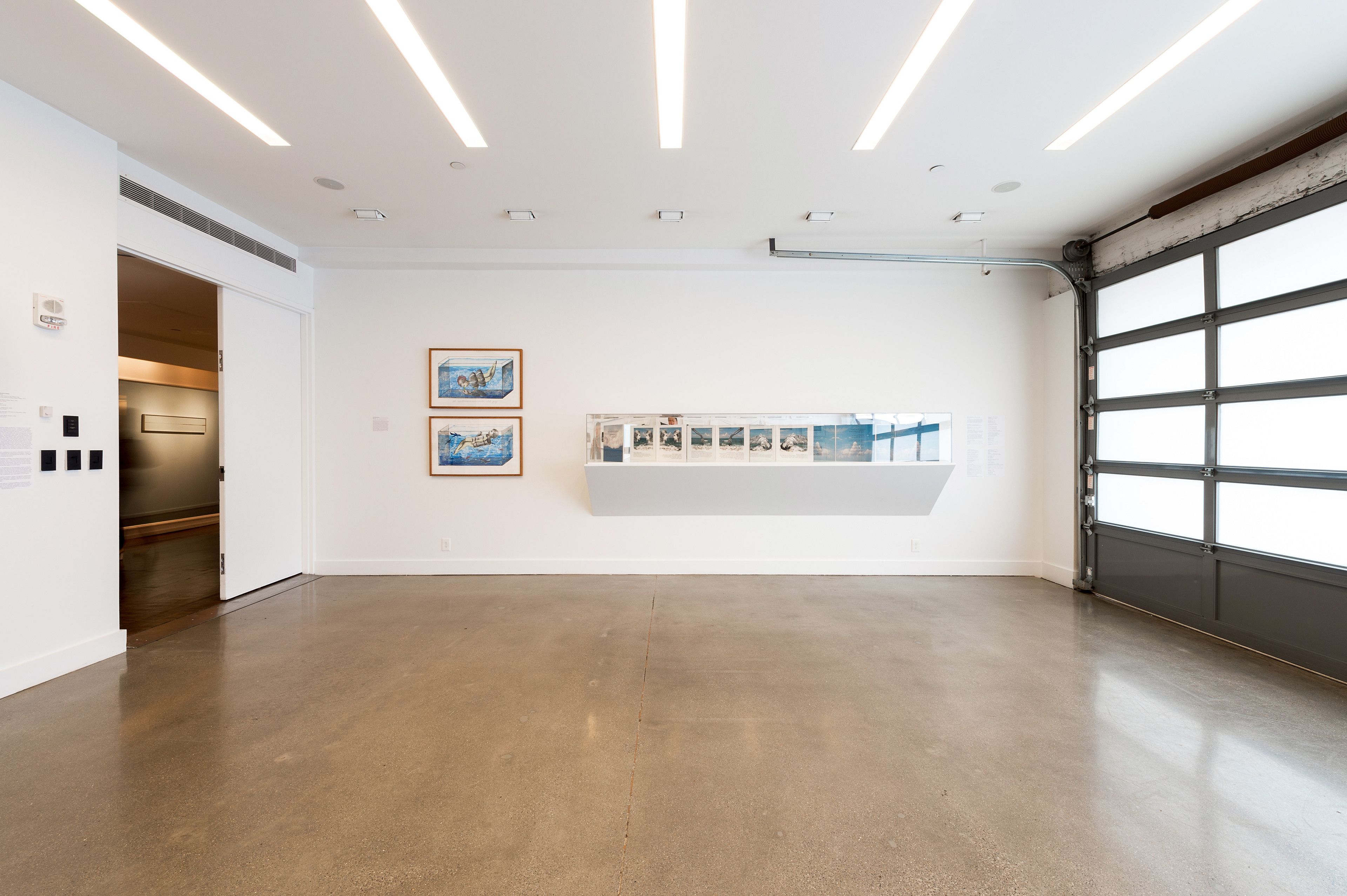 A spacious gallery with a concrete floor, white walls, and a large window.
