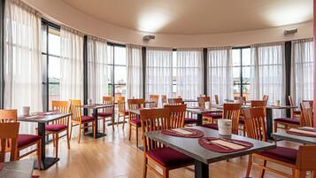 A dining area with round tables, wooden chairs, and red cushions.