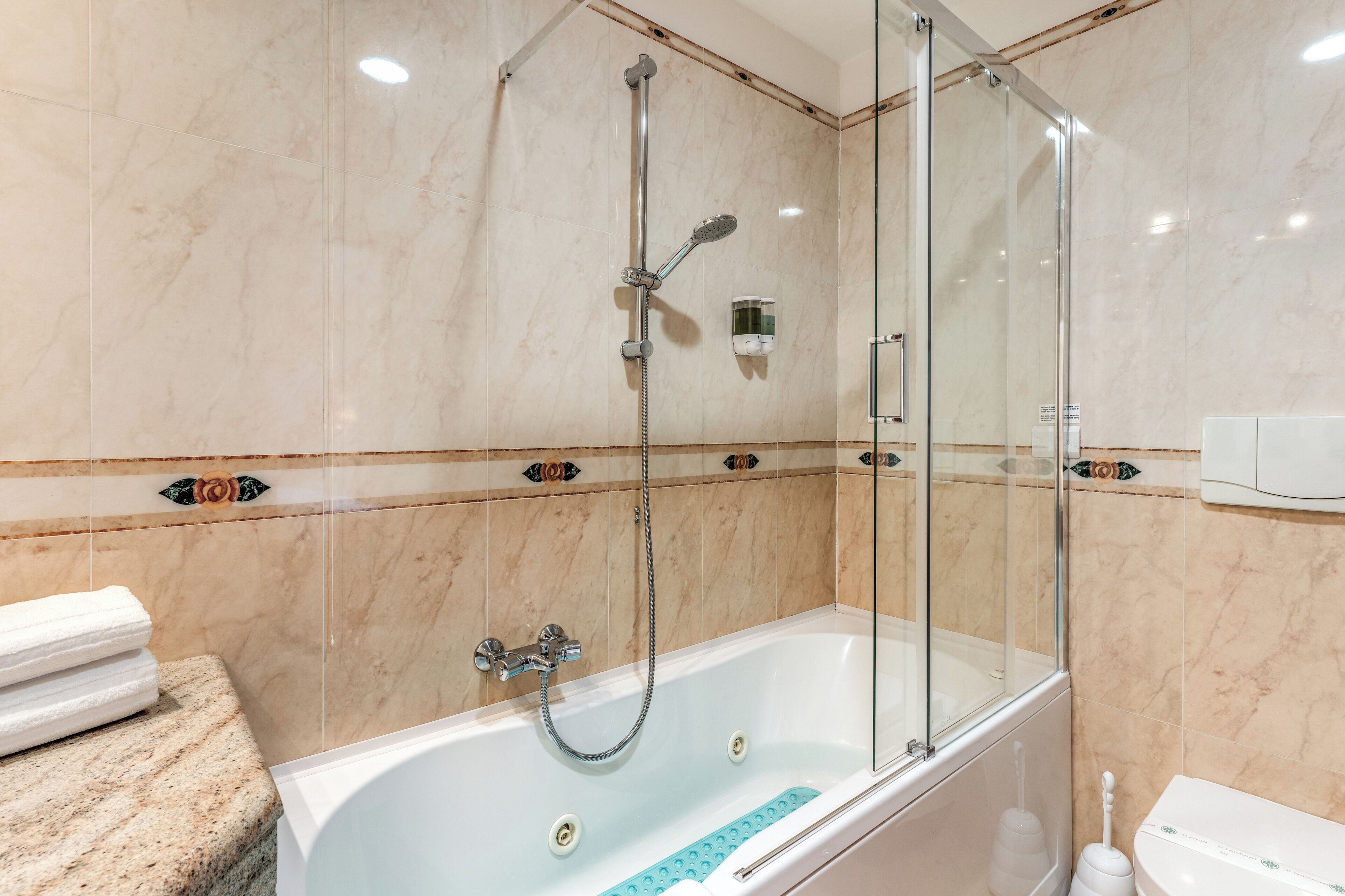 A modern bathroom with a glass-enclosed shower, a white bathtub, and a marble-tiled wall.