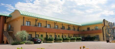 A hotel with a green roof, multiple balconies, and a paved courtyard.