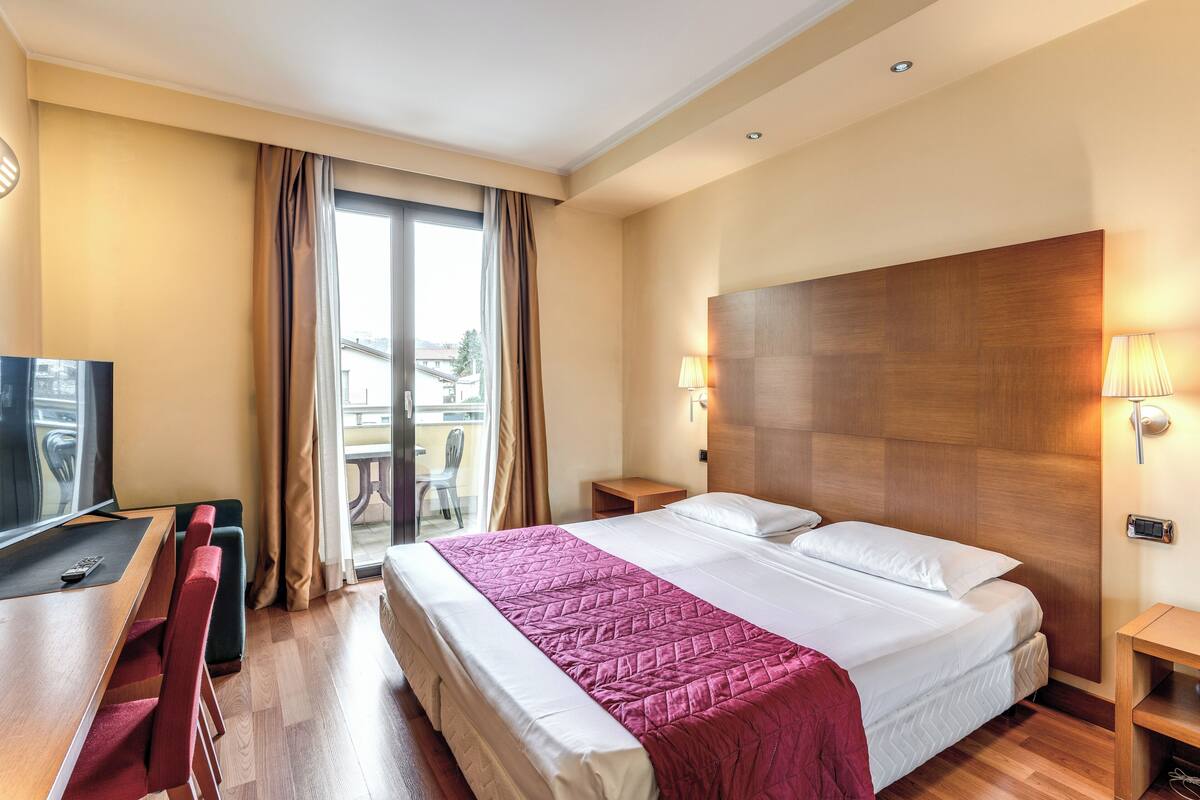 A hotel room with a bed, a desk, a chair, and a TV.