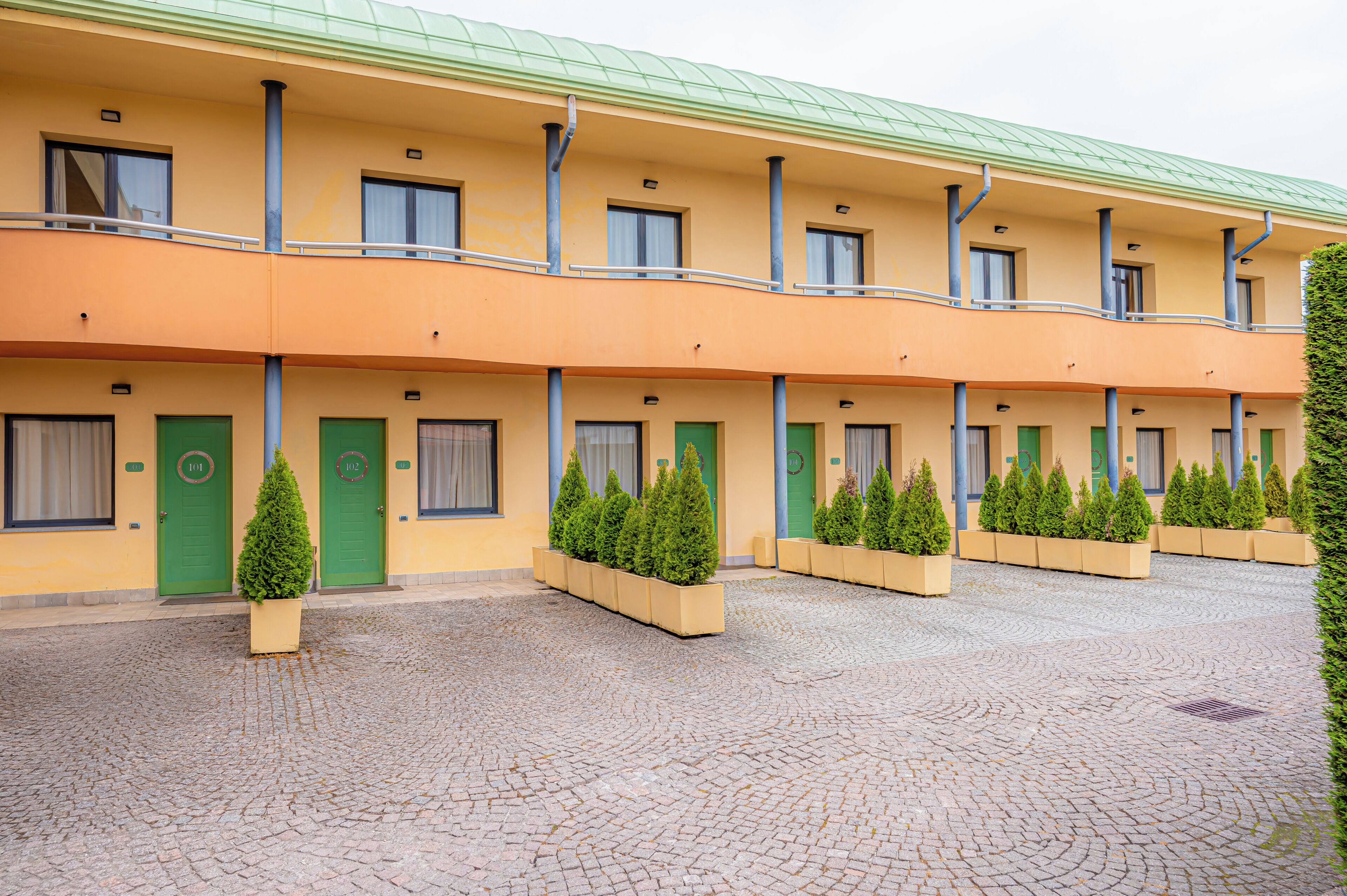 Un hotel con una fila di camere, ognuna con una porta verde e un piccolo albero in vaso di fronte.