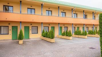 Un hotel con una fila di camere, ognuna con una porta verde e un piccolo albero in vaso di fronte.