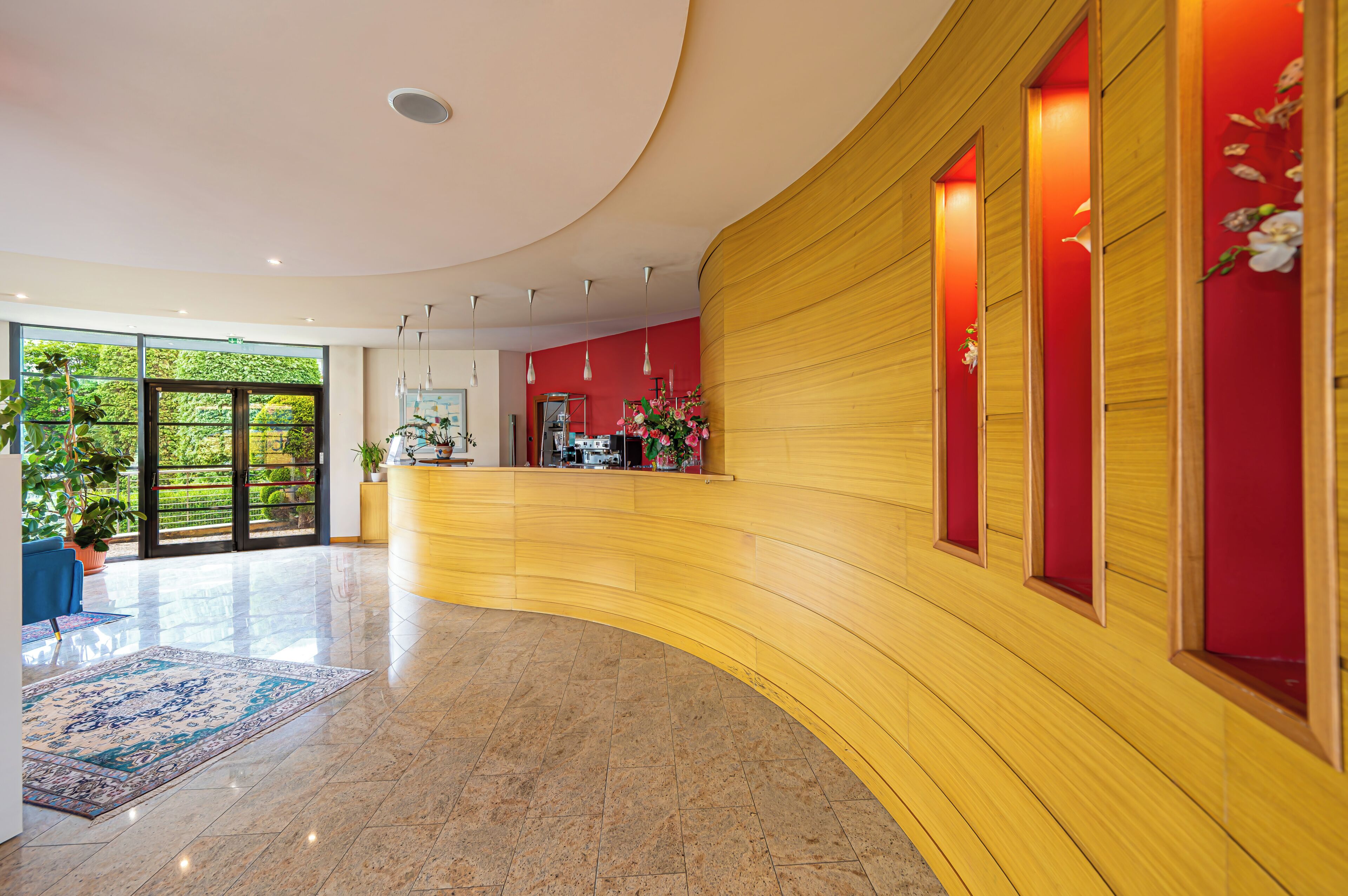 A modern lobby with a curved reception desk, large windows, and a potted plant.