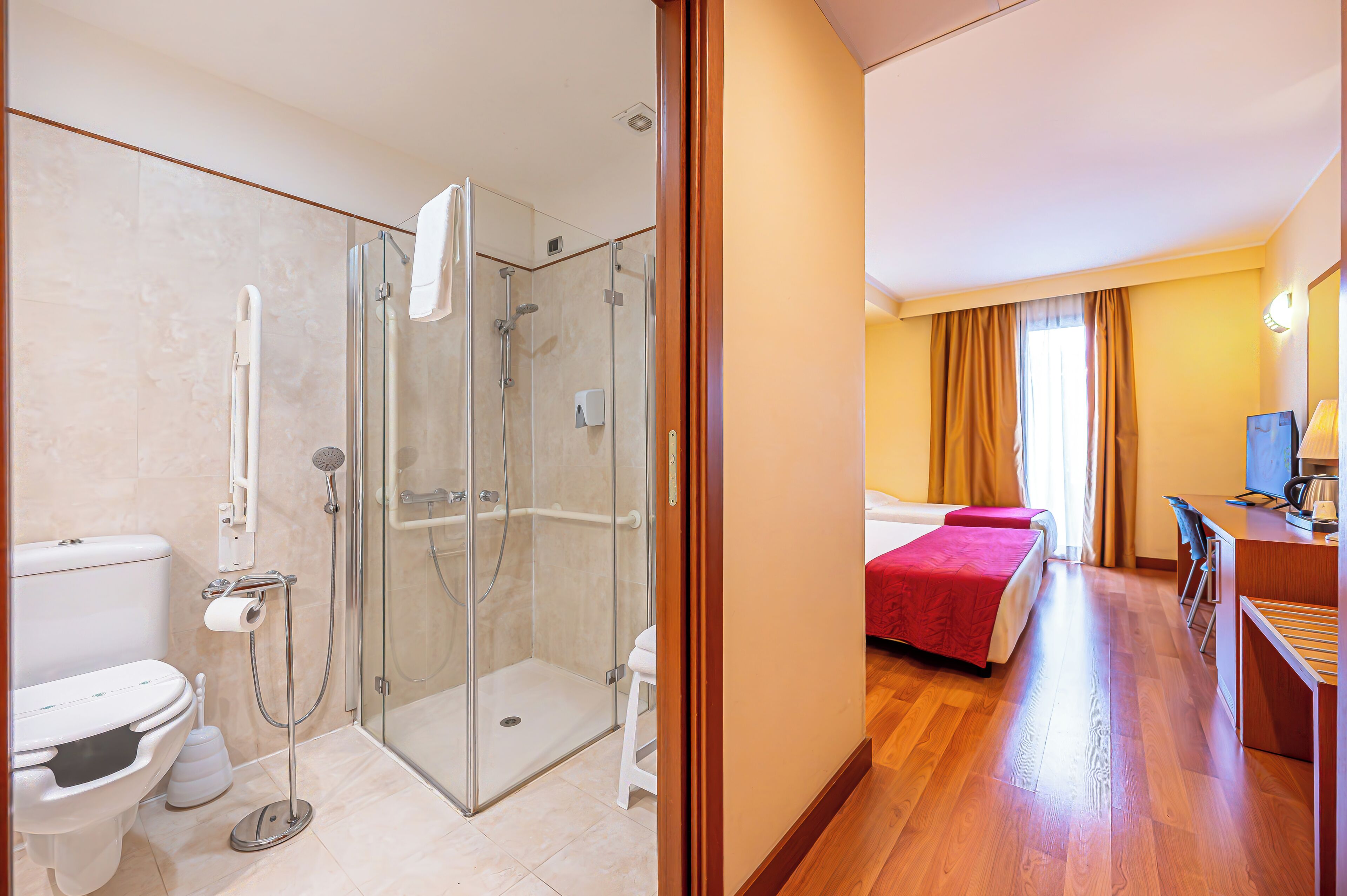 A hotel room with a shower, toilet, bed, and desk area.