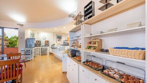 Un bufé de desayuno con diversos alimentos, una zona de estar con sillas y una cocina al fondo.