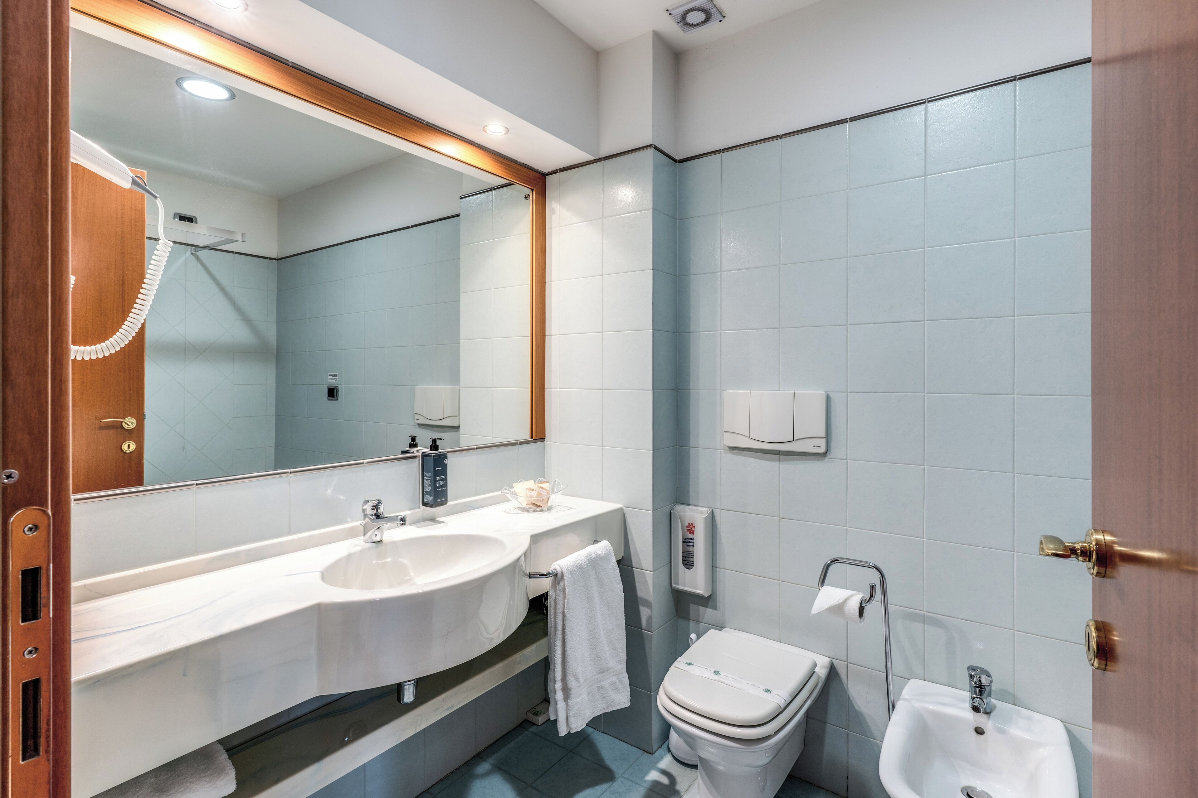 A modern bathroom with a large mirror, two sinks, a toilet, and a bidet.