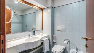 A modern bathroom with a large mirror, two sinks, a toilet, and a bidet.