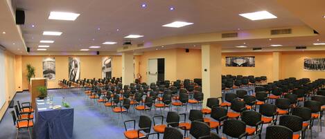 A conference room with rows of chairs, a stage with a podium, and artwork on the walls.