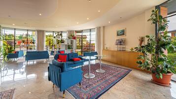 A spacious lobby with blue sofas, a patterned rug, and large windows offering a view of the outside.
