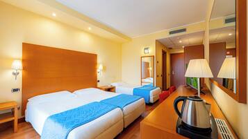 A hotel room with two beds, a desk with a kettle, a TV, and a mirror.