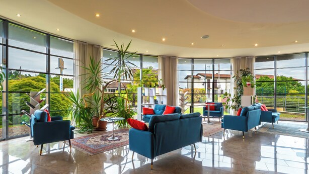 Amplia sala de estar con ventanas grandes, techo alto y mobiliario moderno.
