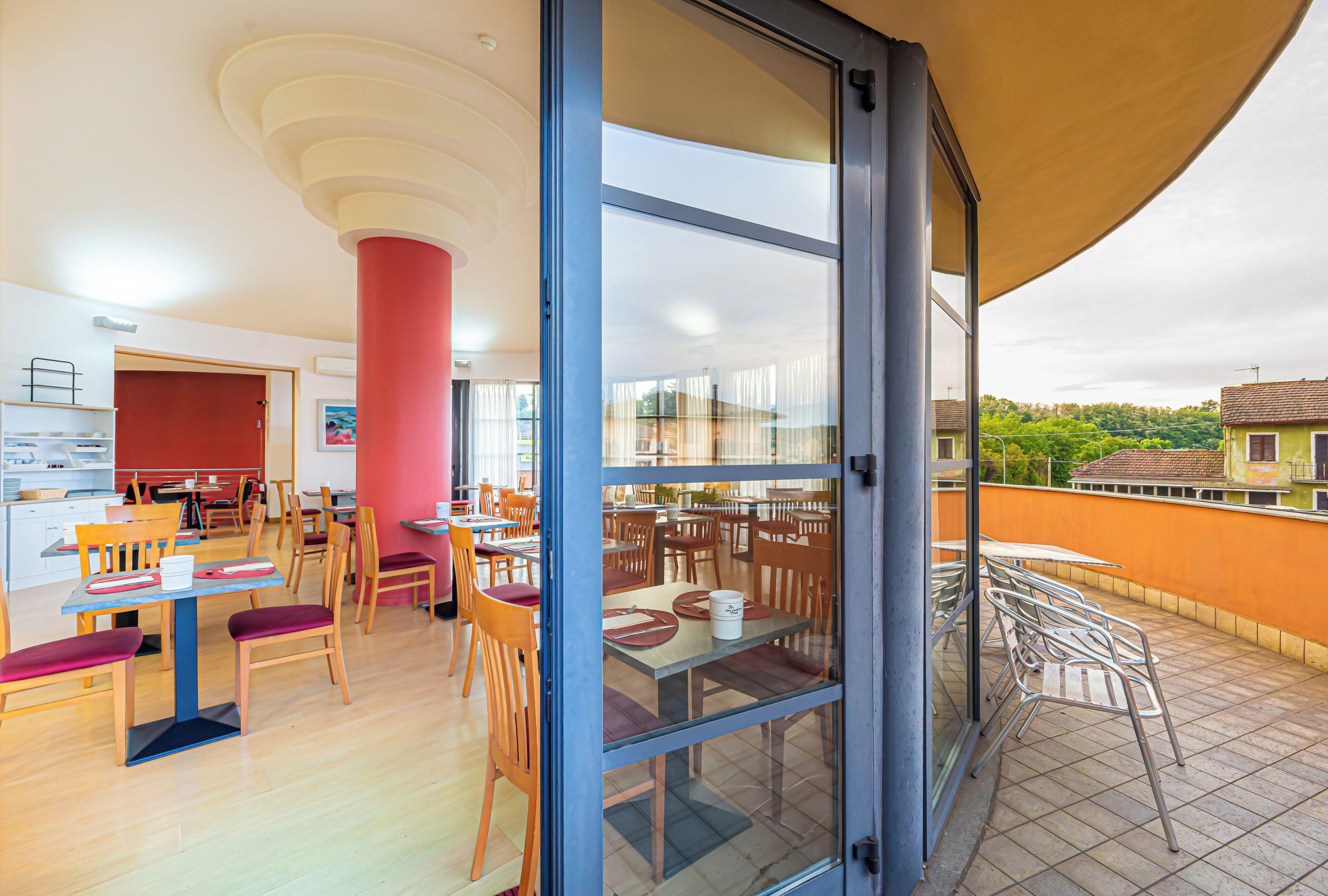Un comedor con mesas y sillas, un pilar rojo y vistas al exterior.