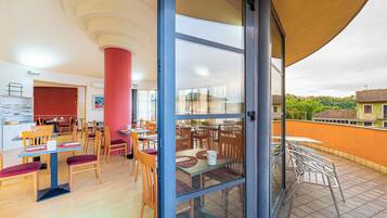 Un comedor con mesas y sillas, un pilar rojo y vistas al exterior.