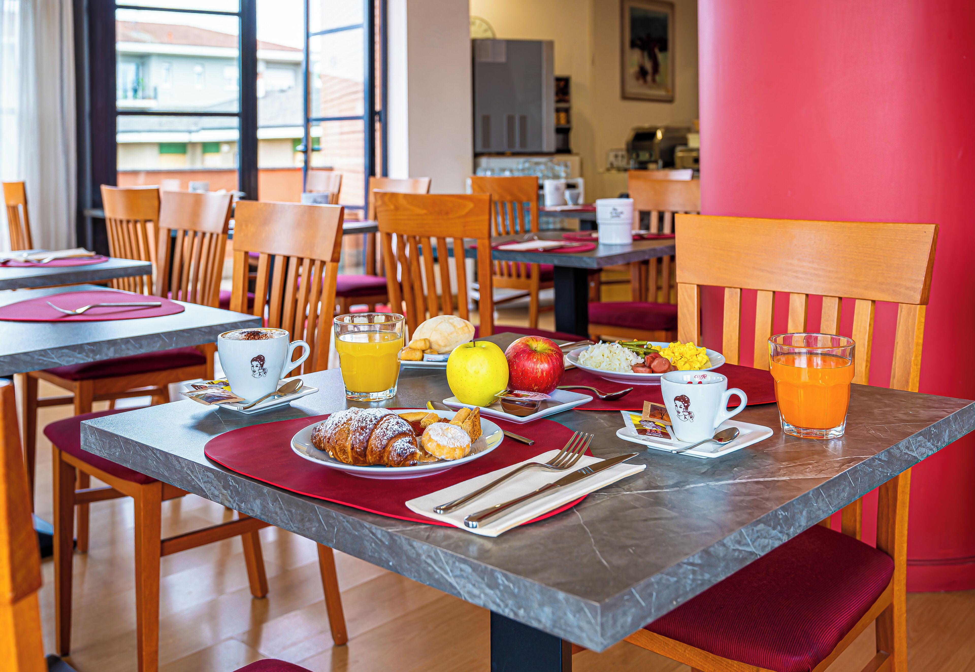 A breakfast setting with tables, chairs, and a variety of breakfast items including pastries, fruits, and beverages.