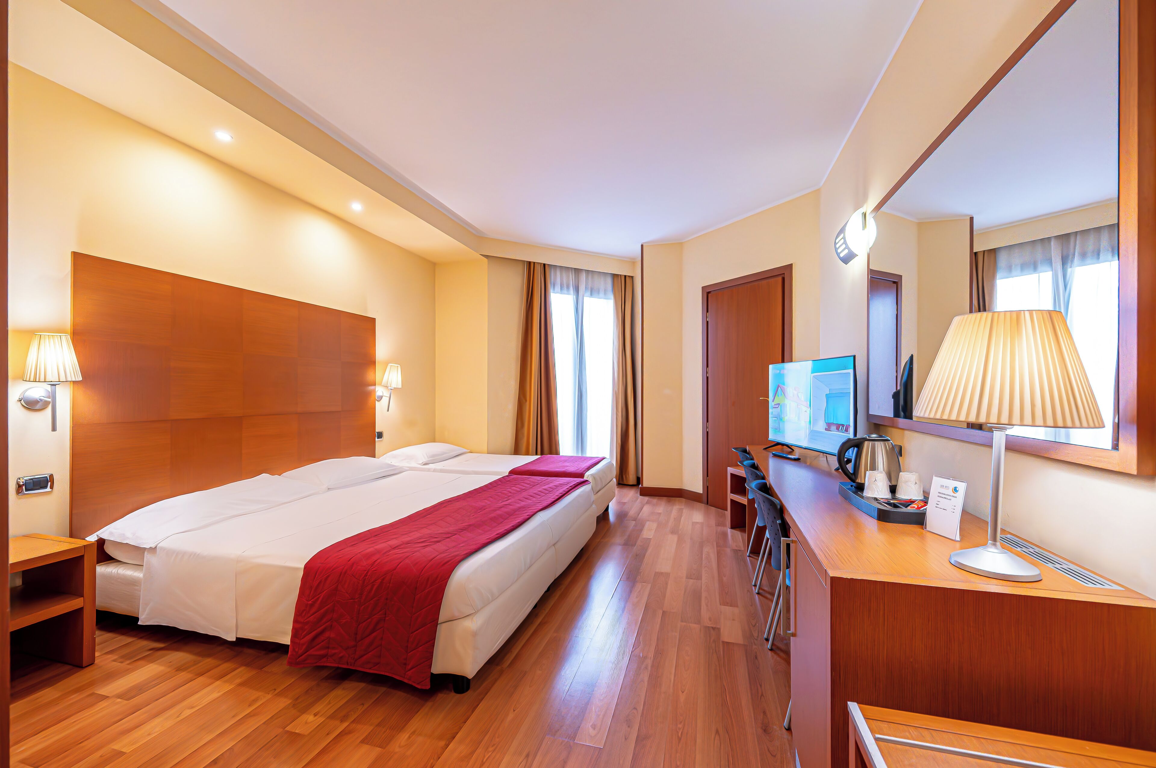 Ein Hotelzimmer mit einem großen Bett, einem Schreibtisch mit Lampe, einem Fernseher und einer Kaffeemaschine.