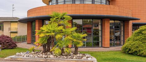 Un edificio moderno con fachada curva, grandes ventanales y un jardín ajardinado con palmeras.