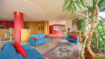 A modern lobby with blue sofas, a red reception desk, and a large potted plant.