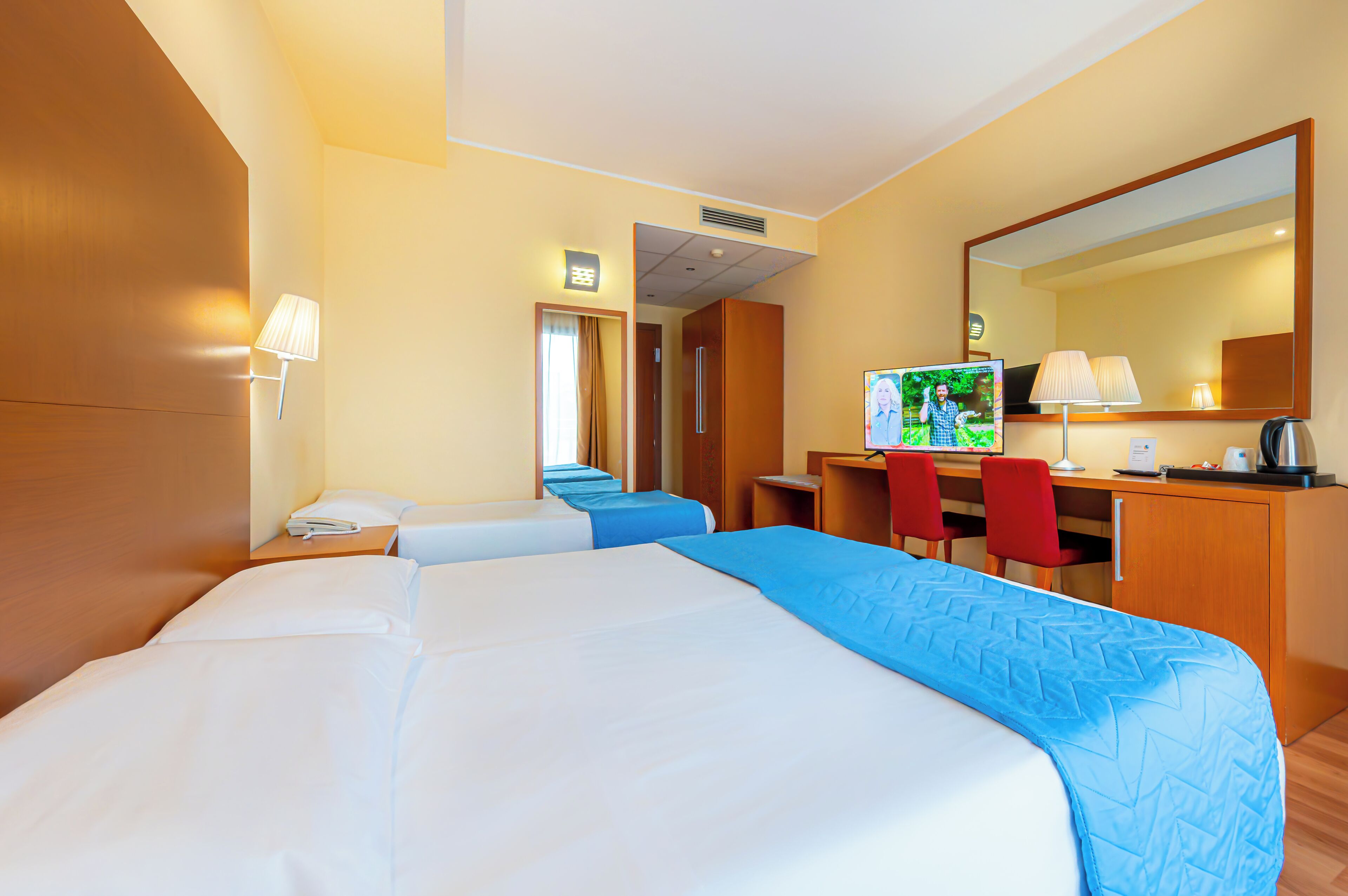 Een hotelkamer met twee bedden, een bureau, een stoel, een televisie en een spiegel.