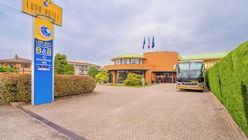 Entrada de hotel con un letrero, camino pavimentado y un autobús estacionado.