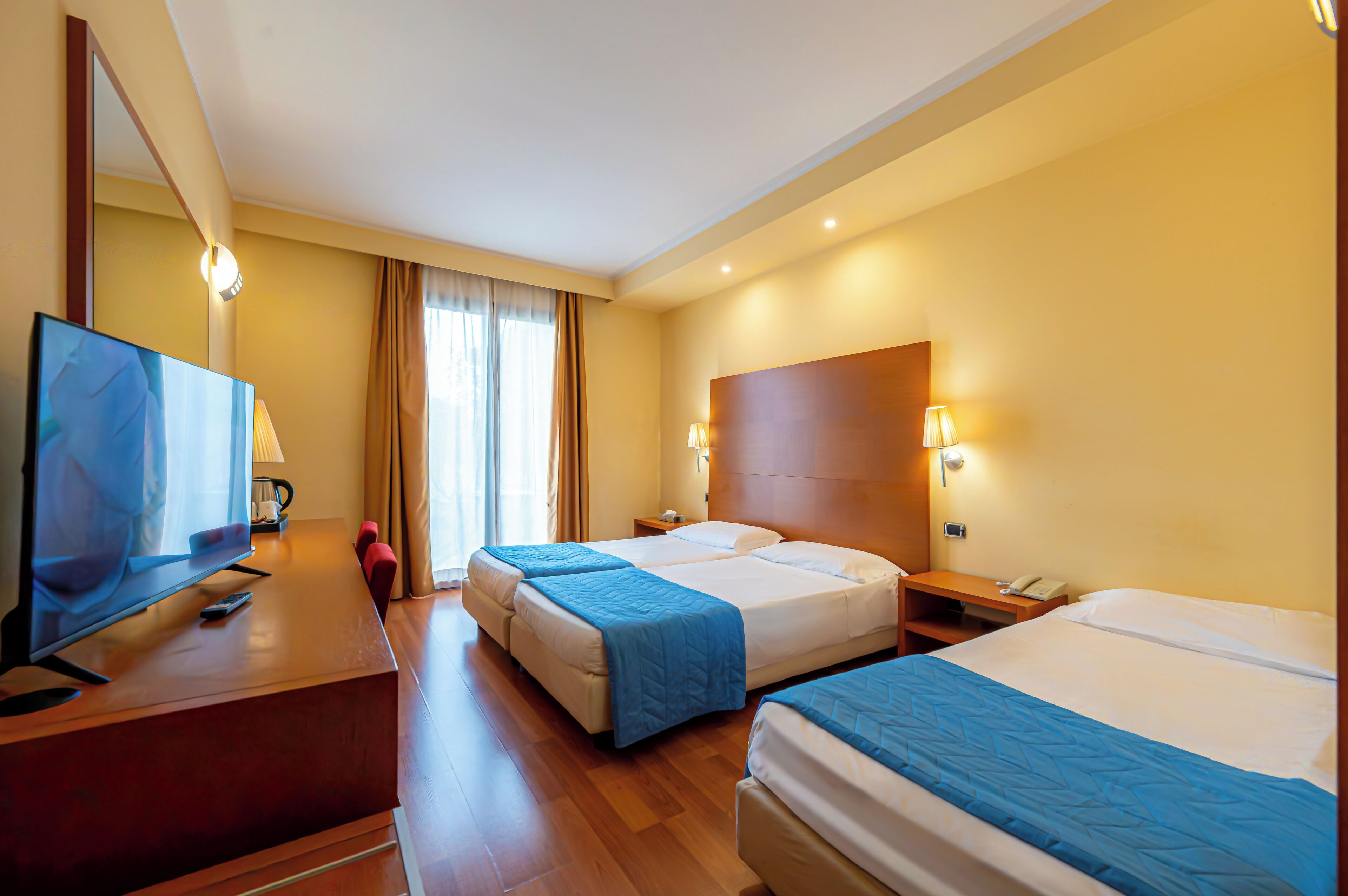 A hotel room with two beds, a TV, a desk, and a mirror.