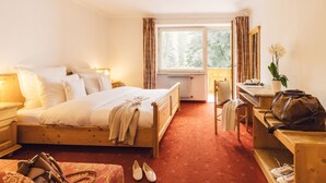 A hotel room with a wooden bed, a desk, a chair, a radiator, and a window with curtains.