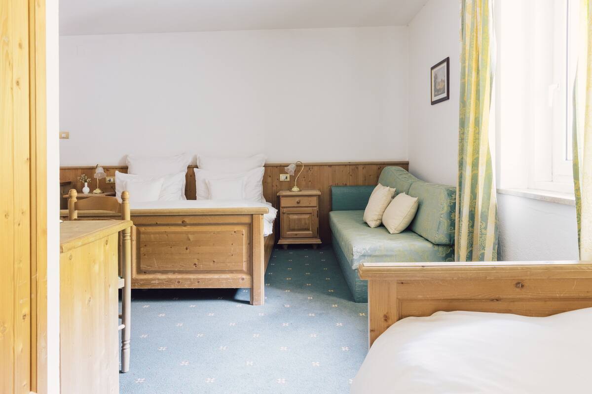 Een slaapkamer met een houten bed, een nachtkastje van hout, een groene bank en een raam met gordijnen.