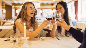 Two people toasting with wine glasses at a table with a candle, in a warmly lit dining area.