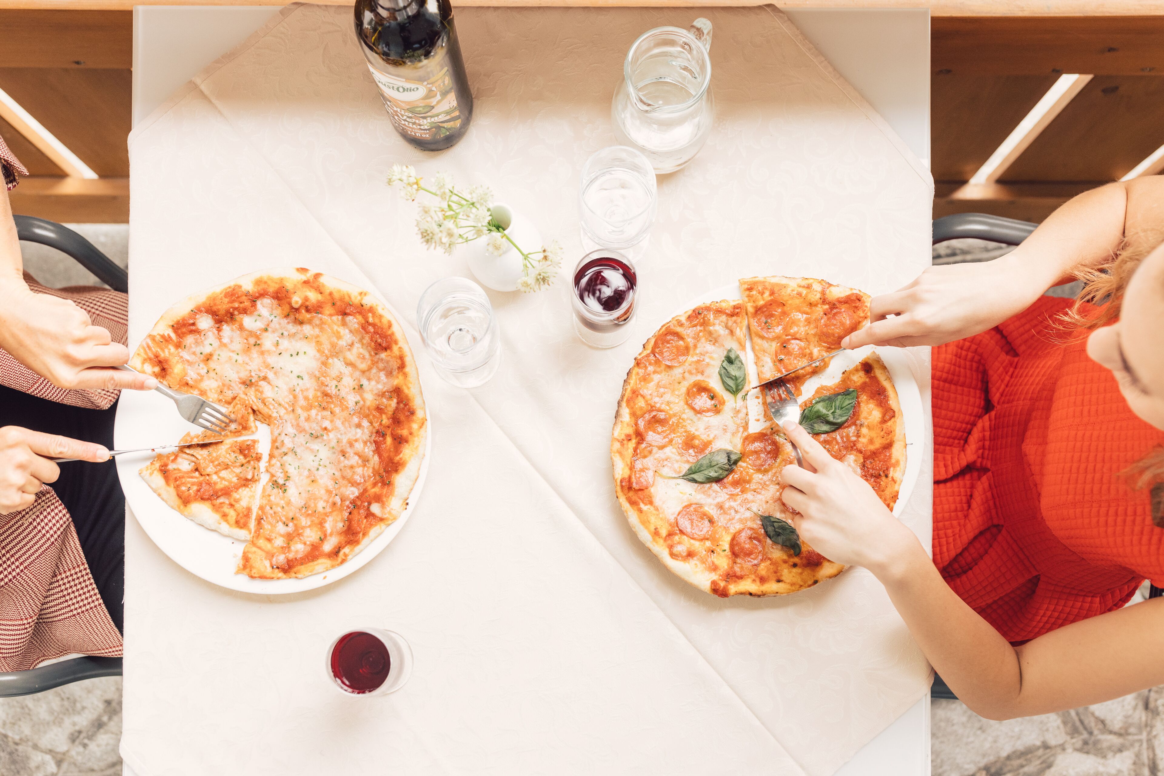 Una mesa con dos pizzas, una botella y vasos de agua y vino tinto.