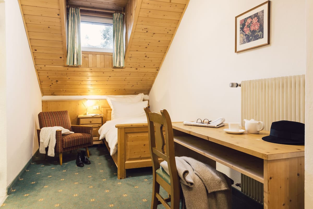 Een gezellige kamer met schuine kap, een bed, een stoel, een bureau en een radiator.