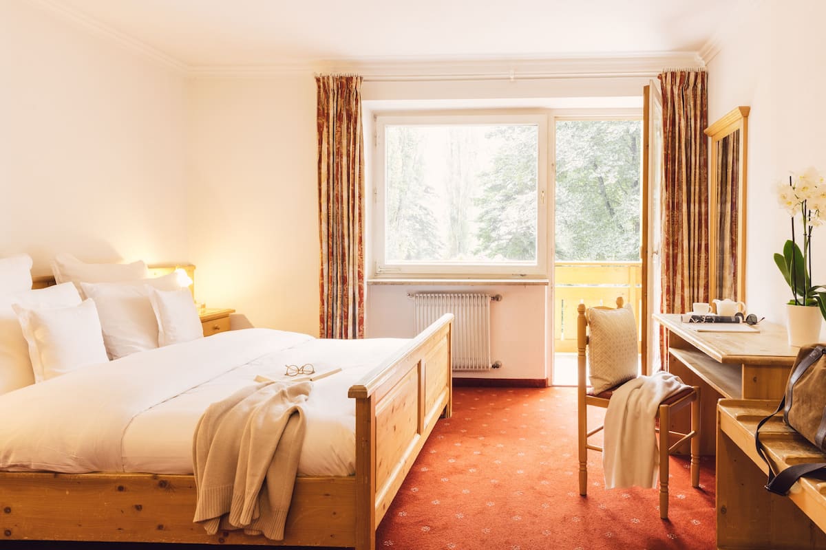 Een hotelkamer met een bed, een bureau, een stoel, een radiator en een raam met gordijnen.