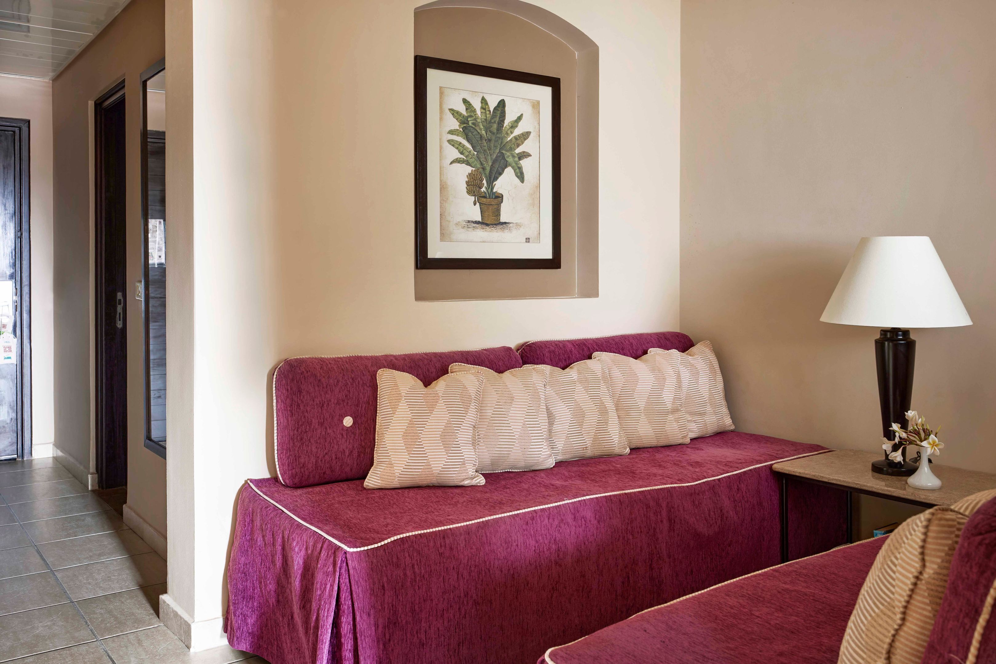 A room with a sofa, a framed botanical illustration, a lamp, and a small table with a vase.