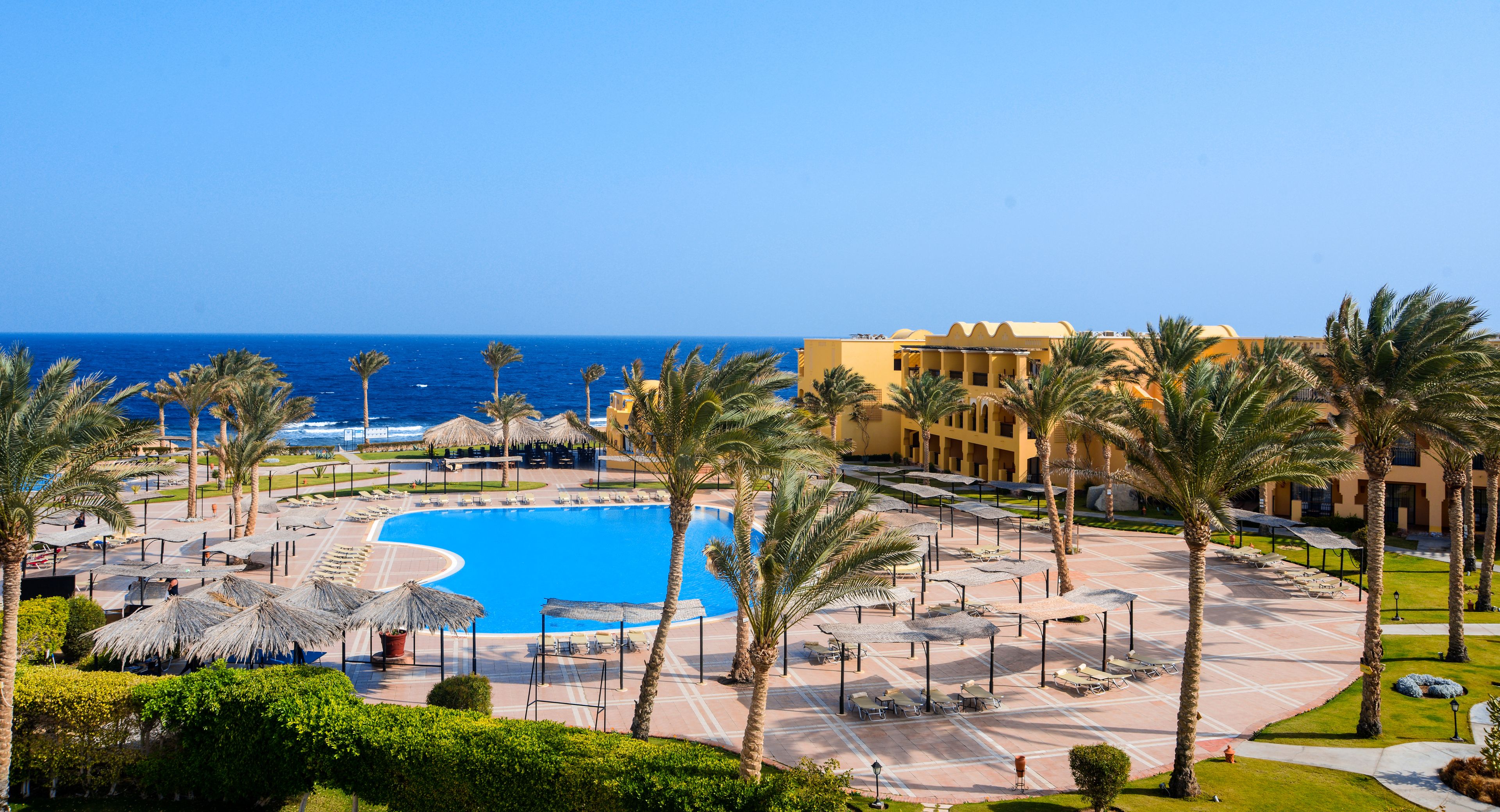 A resort with a large pool, palm trees, and a view of the ocean.