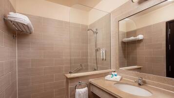 Un baño moderno con cabina de ducha de vidrio, lavabo con artículos de aseo y un espejo grande.