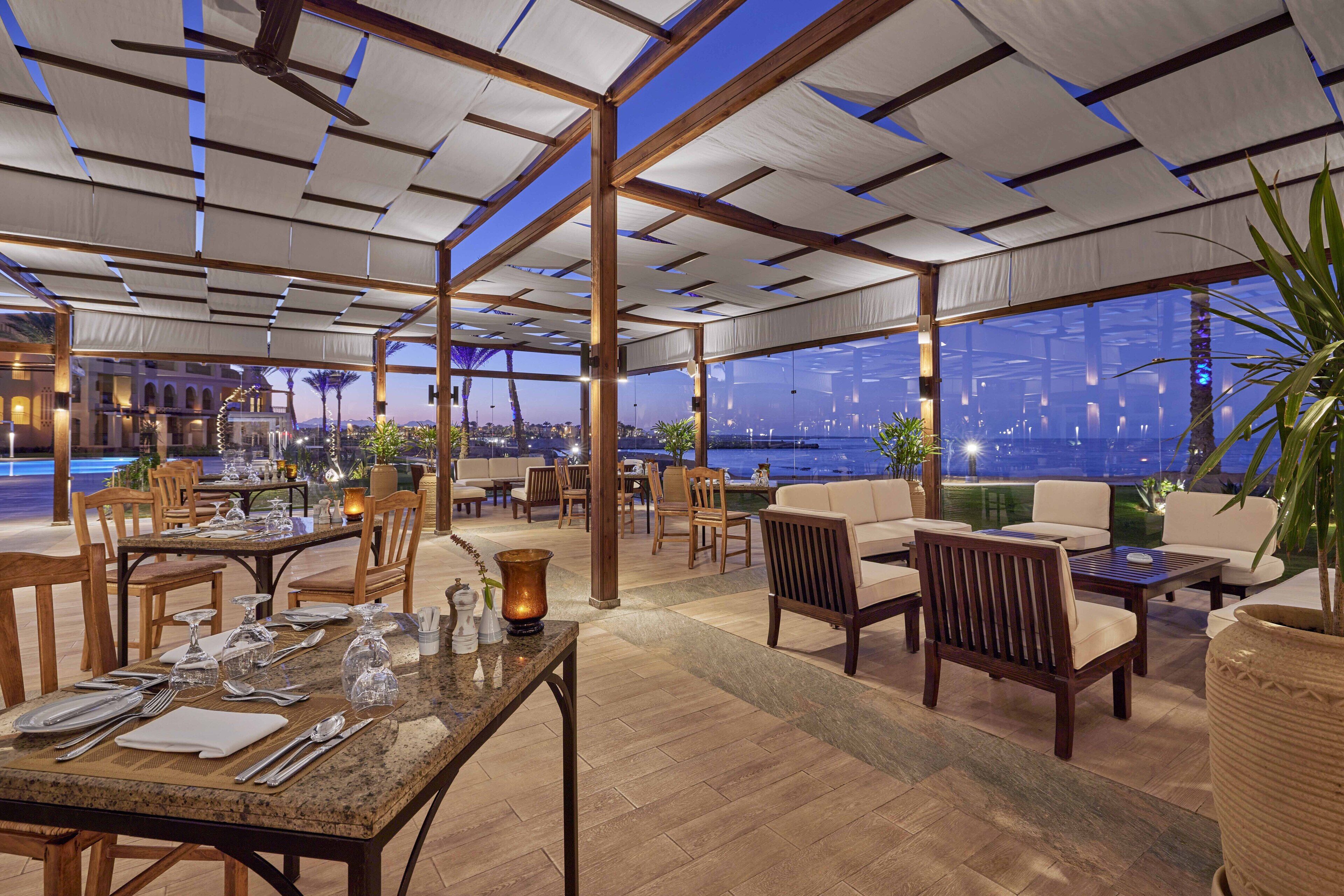 A restaurant with outdoor seating, wooden tables, and chairs, and a view of the cityscape at night.
