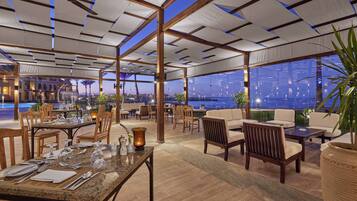 A restaurant with outdoor seating, wooden tables, and chairs, and a view of the cityscape at night.