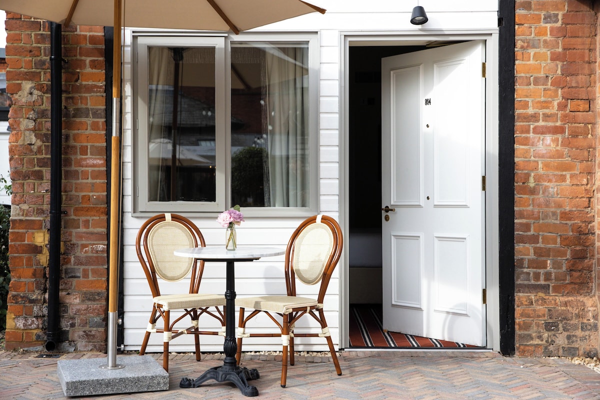 Un patio con una mesa y dos sillas de mimbre, una puerta blanca y un muro de ladrillo.