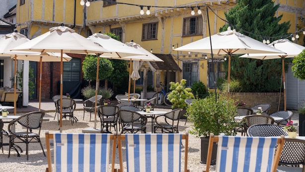 An outdoor seating area with tables and chairs, umbrellas, and string lights. - The Relais Henley (Henley-on-Thames)