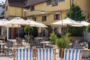An outdoor seating area with tables and chairs, umbrellas, and string lights. - The Relais Henley (Henley-on-Thames)