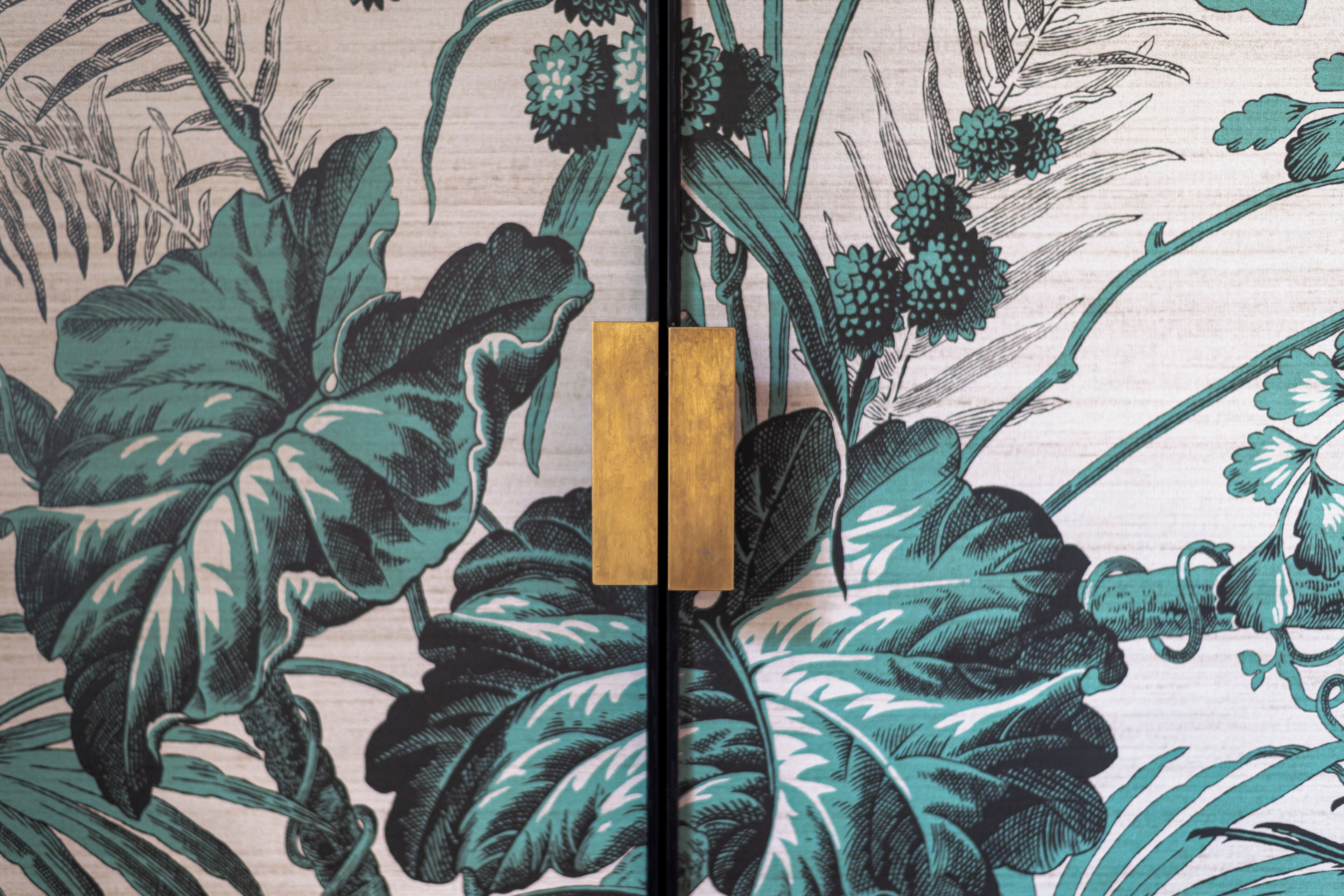 A room with a large window, a wooden door, and a floral wallpaper pattern.