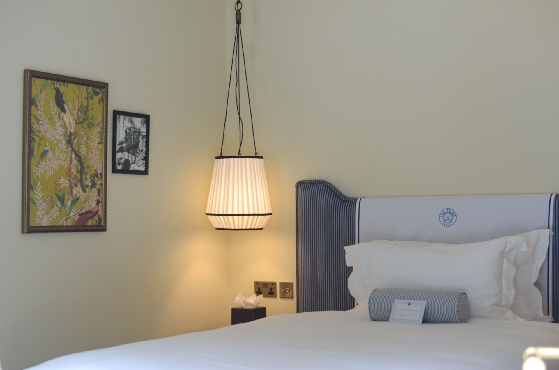 A hotel room with a bed, a nightstand, a lamp, and two framed pictures on the wall.