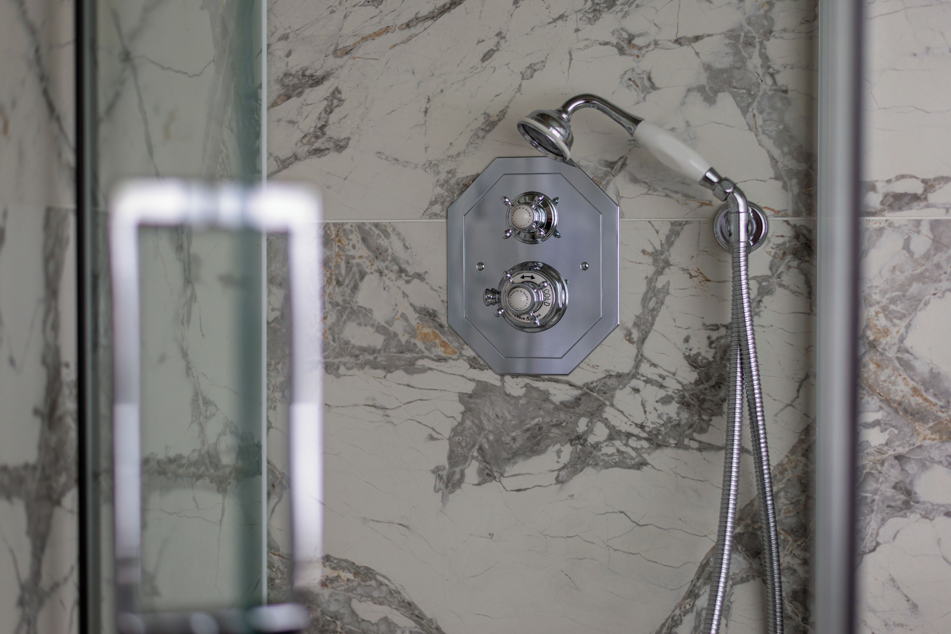 Une douche équipée d’un pommeau de douche à main et d’un pommeau de douche fixe, le tout installé sur un mur en marbre.