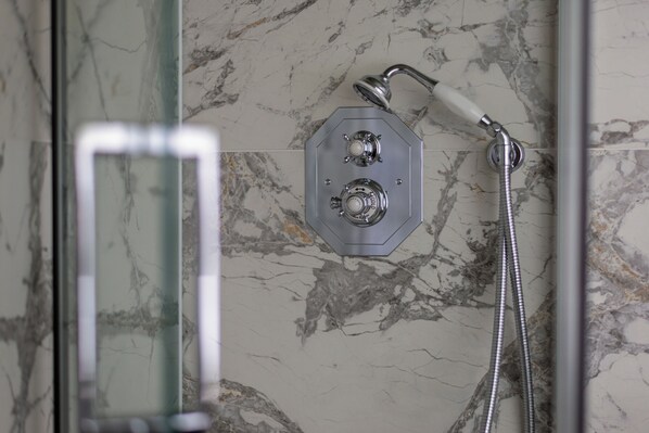 A shower with a handheld showerhead and a fixed showerhead, set against a marble wall.