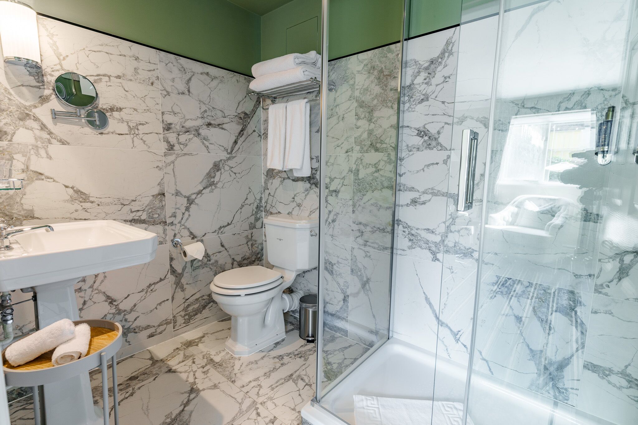 Un baño moderno con suelo de mármol, ducha con cerramiento de vidrio, lavabo blanco y un inodoro.
