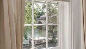 A window with a view of a bridge over water, curtains, and a lock on the window frame. - The Relais Henley (Henley-on-Thames)