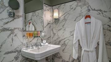 Un baño con pared de mármol, un lavamanos, un espejo, una bata colgada y un perchero para toallas.