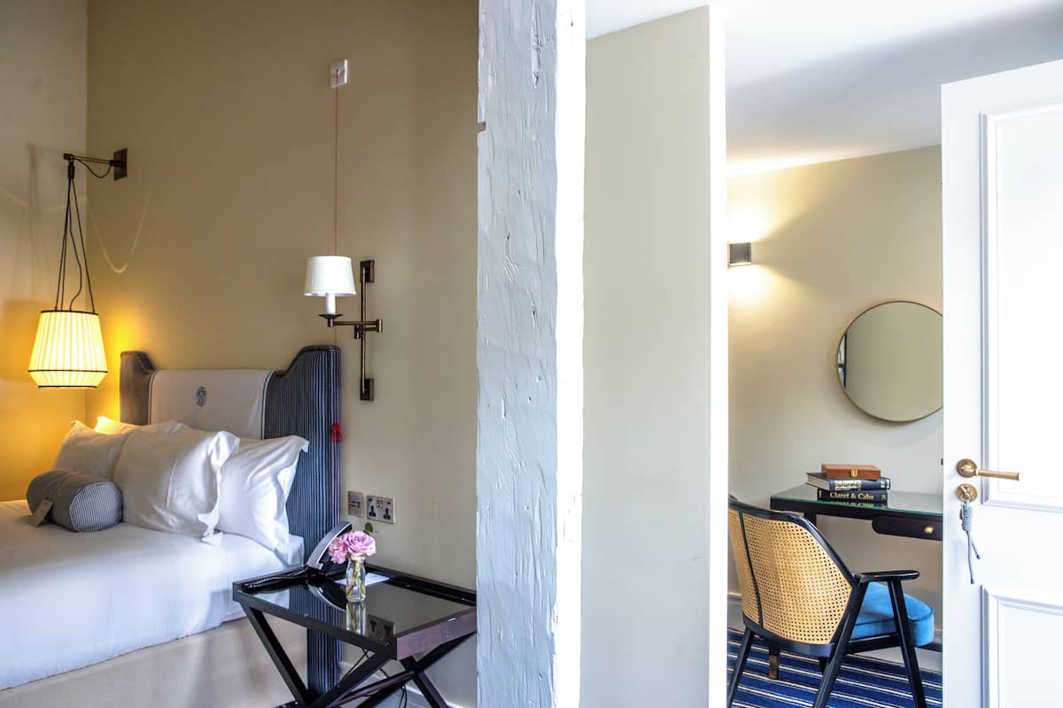 A hotel room with a bed, a desk, a chair, a lamp, and a mirror.